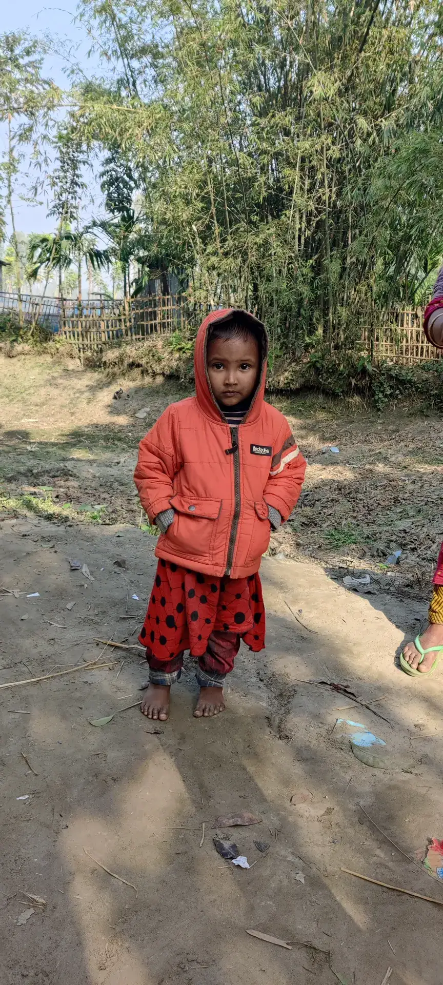 A small girl in a warm red outfit on a village path.