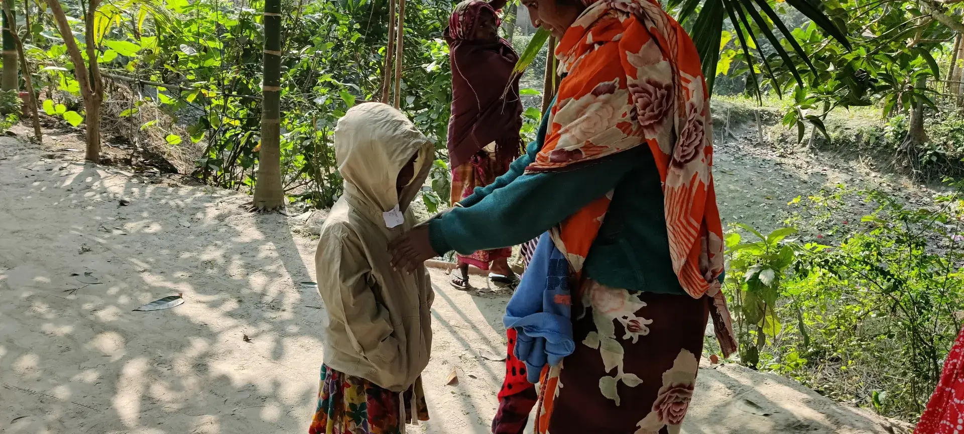 A woman helps a child in a warm hooded jacket on a village path.