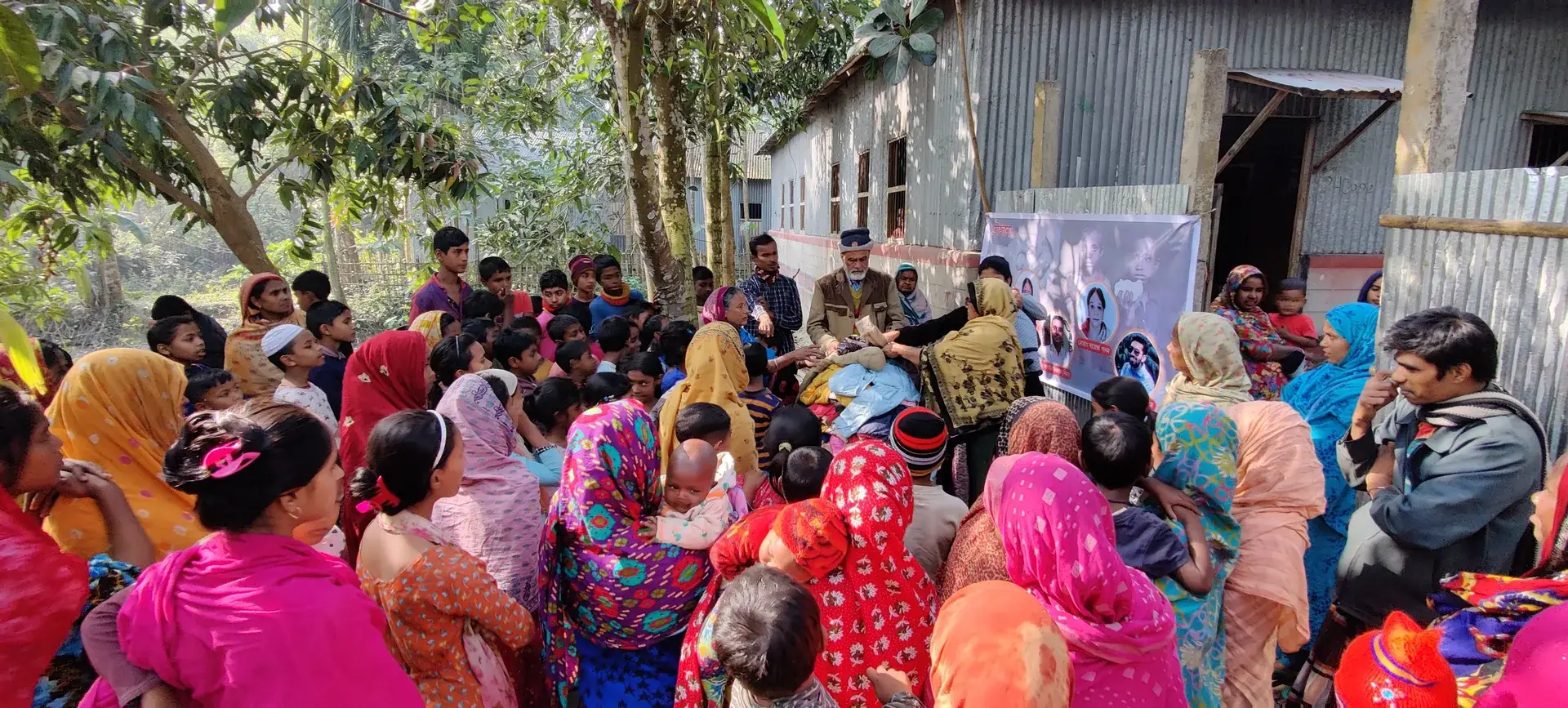 A crowd of villagers, many women in colourful saris, gathered under the trees.