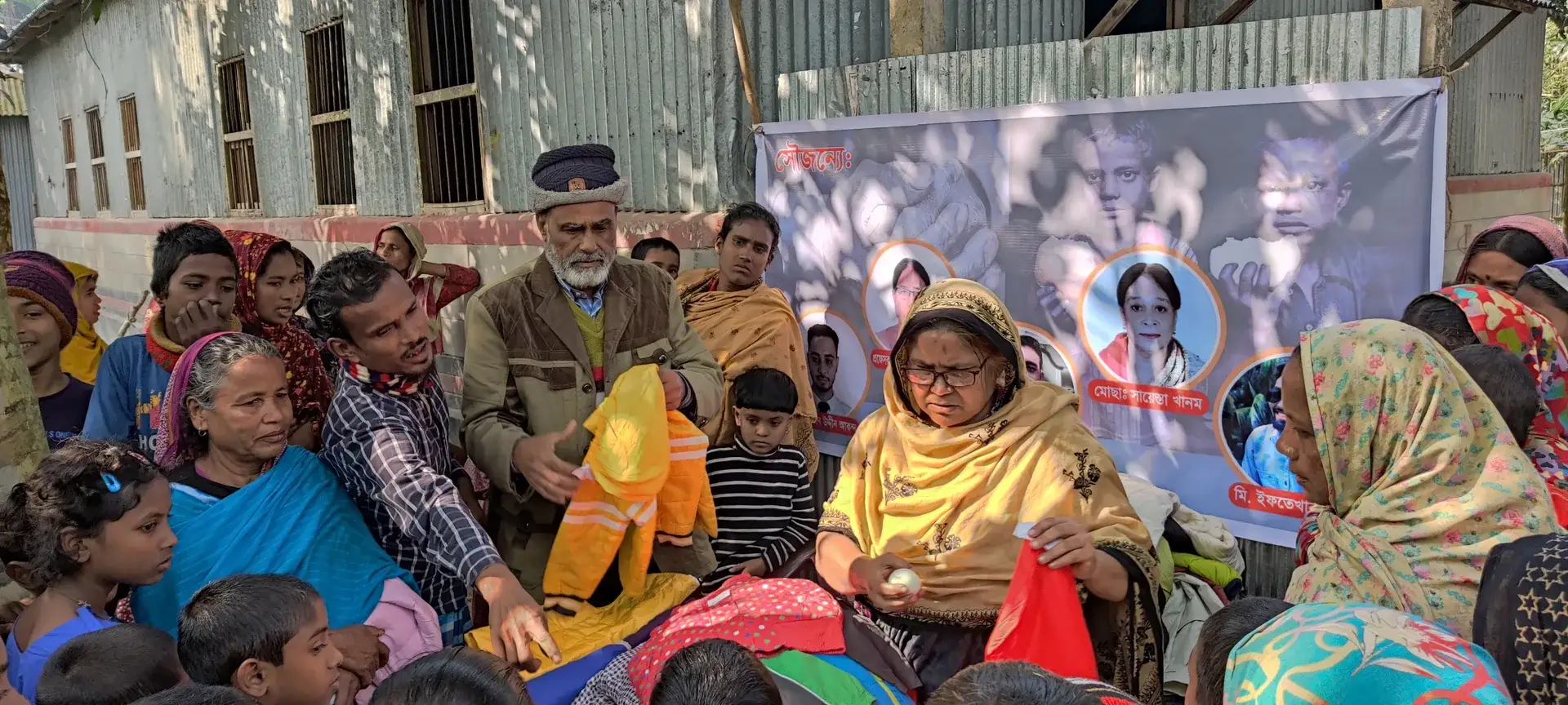Women and elders seated together in front of a banner at the distribution.